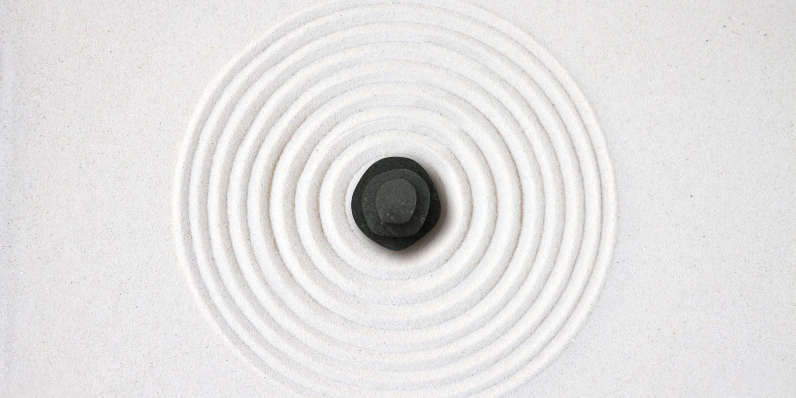 Galet noir sur cercle en sable blanc épuré illustrant le minimalisme appliqué aux soins naturels certifiés COSMOS NATURAL ou ORGANIC – KALYAË ORIGIN