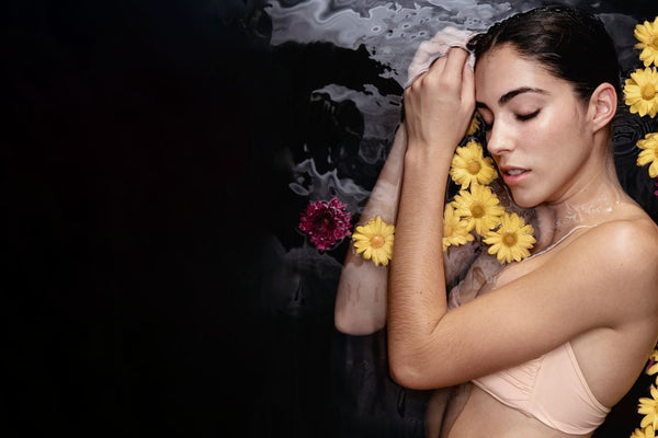 Femme apaisée entourée de fleurs, illustrant la sensorialité des soins naturels certifiés COSMOS NATURAL ou ORGANIC – KALYAË ORIGIN