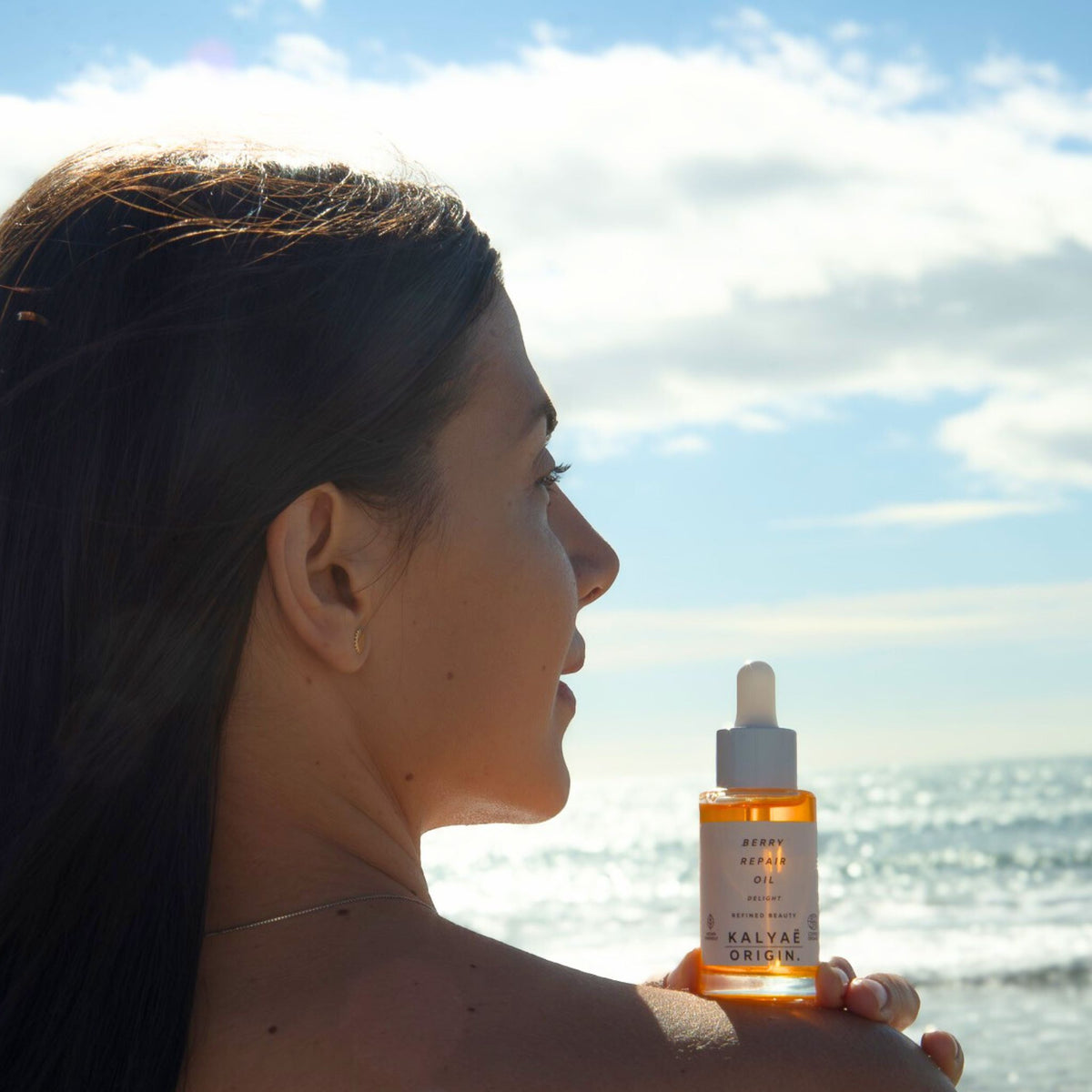 Berry Repair Oil huile régénérante visage certifiée COSMOS NATURAL 30 ml présentée en application en extérieur près de la mer – KALYAË ORIGIN