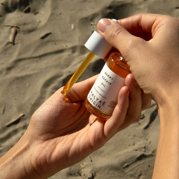 Berry Repair Oil huile régénérante visage certifiée COSMOS ORGANIC 30 ml présentée en application en extérieur sur le sable – KALYAË ORIGIN