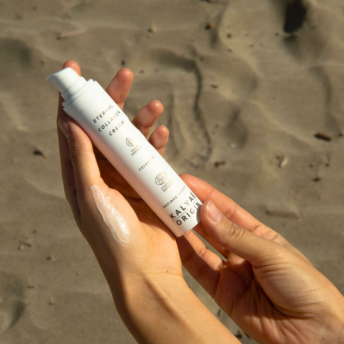 Eternal Collagen Cream crème raffermissante visage certifiée COSMOS NATURAL 50 ml présentée en application sur le sable en extérieur – KALYAË ORIGIN